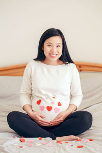 Chinese pregnant woman sitting on bed touching her belly. pregnant belly covered with red hearts