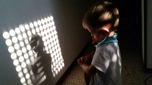 Side view of boy playing with shadow on wall at home