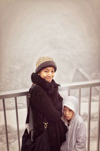 Portrait of smiling woman with son by railing during winter