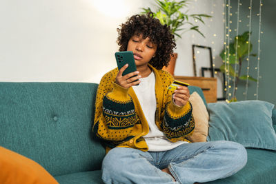 Young woman using mobile phone while sitting on sofa at home