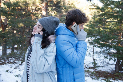 Couple talking on mobile phone while standing on snow covered field