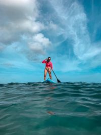 Woman paddleboarding in sea against sky