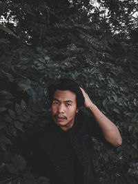 Asian male model poses tree background surrounded by leaves moody dark sunlight behind on the face