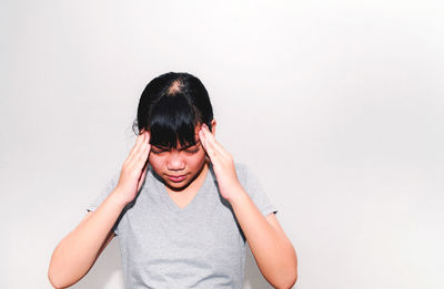 Portrait of young woman covering face against white background