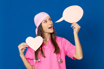 Portrait of woman holding pink heart shape against blue sky