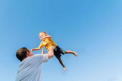 Happy father throwing up baby against blue sky