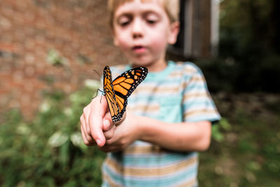 Monarch butterfly sitting on boy's hand as he observes it