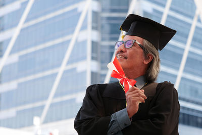 Businessman in graduation gown standing against office building