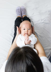 Young woman holding asian baby sitting on bed at home, asian mom and baby, smile, motherhood