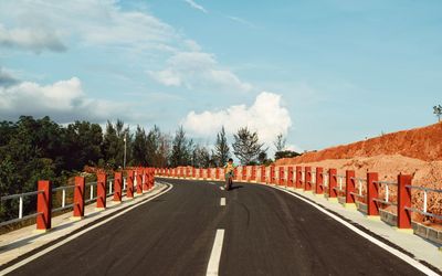 Boy riding bicycle on road against sky during sunny day