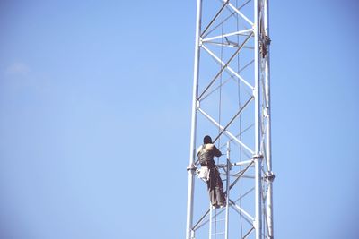 Rear view of worker on pole against blue sky