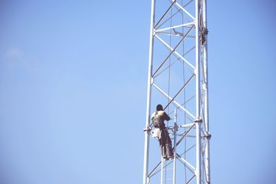 Low angle view of man working against clear blue sky