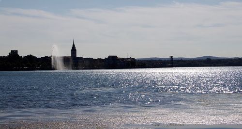 City at waterfront against cloudy sky