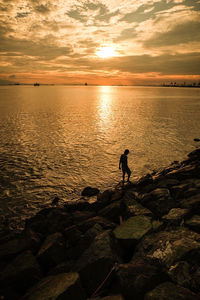 Silhouette man in sea against sky during sunset