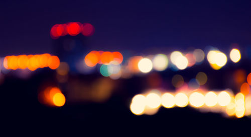 Defocused image of illuminated lights against sky at night