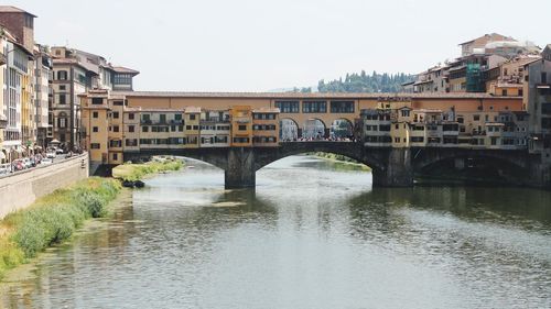 Arch bridge over river amidst buildings against clear sky