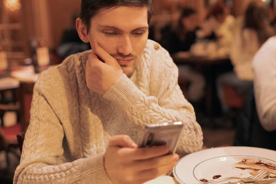 Portrait of a young guy with a phone sitting at the table.