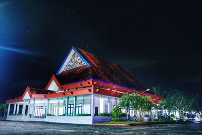Illuminated house by building against sky at night