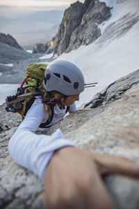 Female rock climber with helmet reaches for a hold on side of cliff