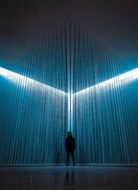 Rear view of silhouette man standing against illuminated wall in building
