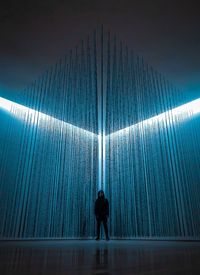 Rear view of silhouette man standing against illuminated wall in building