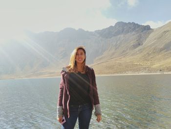Portrait of smiling young woman standing against lake and mountains