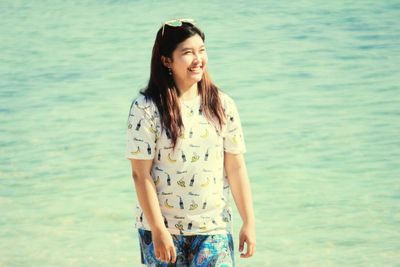 Smiling young woman standing against sea at beach