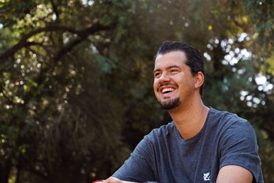 Portrait of young man looking away against trees