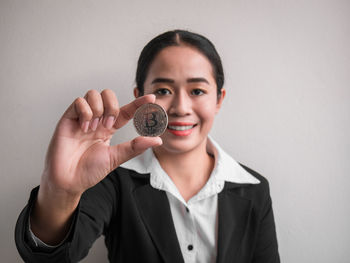 Portrait of smiling businesswoman holding bitcoin while standing against wall