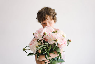 Cheerful happy child with peonys bouquet. smiling little boy on white background.