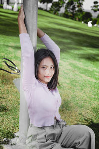 Portrait of smiling young woman sitting on grass against trees