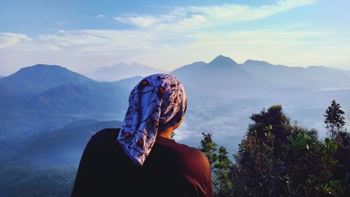 Rear view of man standing on mountain against sky