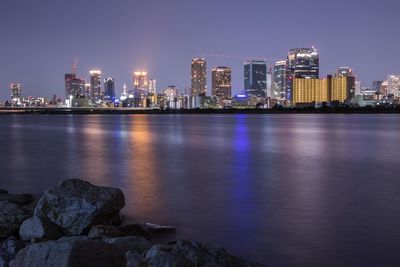 Illuminated buildings by river against sky at night