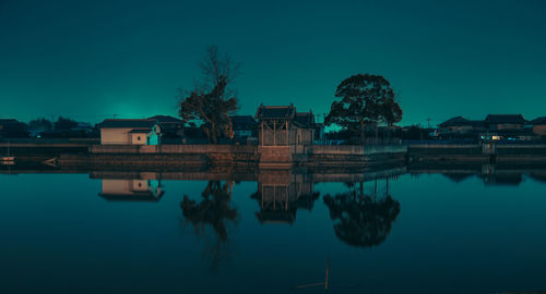 Reflection of houses and trees in river against blue sky at dusk