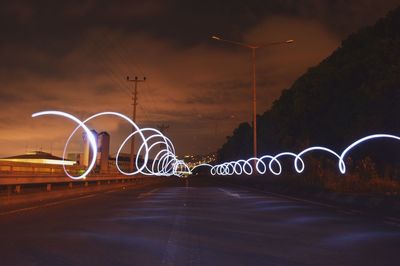 Illuminated light painting on road against sky at night