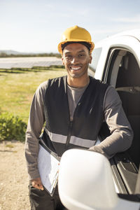 Portrait of confident male engineer holding clipboard while leaning on van door at power station