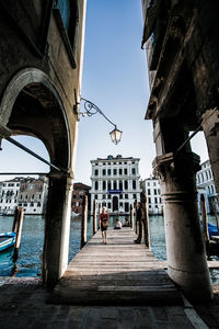 People on pier over canal against buildings