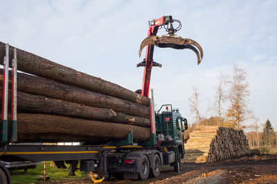 Crane loading logs on vehicle at lumberyard