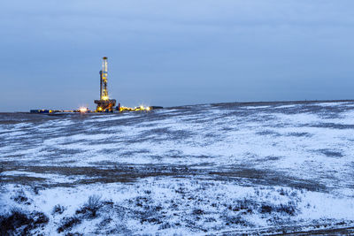 View of oil rig on snow covered land against sky