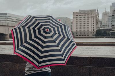 Rear view of an unidentifiable woman with an umbrella standing by the river thames in london, uk.