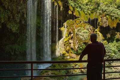 Rear view of man standing at observation point against waterfall