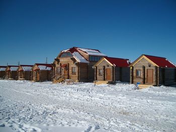 Houses on snow covered field by buildings against clear blue sky