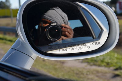 Reflection of man photographing through camera in side-view mirror