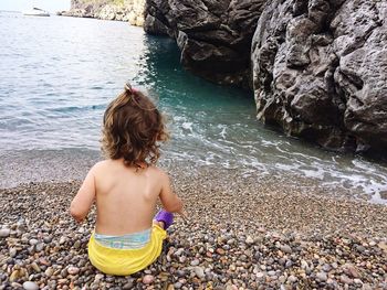 Rear view of girl sitting on pebbles at seashore