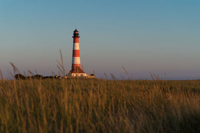 Lighthouse on field against sky during sunset