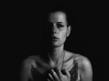 Close-up of shirtless young woman against black background