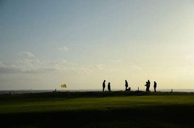 Silhouette people on golf course against sky during sunset