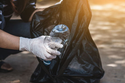 Midsection of woman picking crushed plastic bottle from road