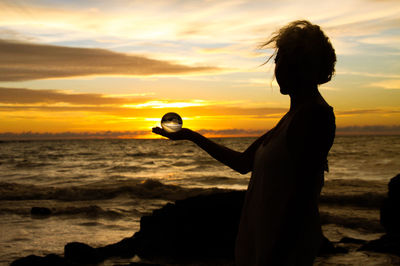 Silhouette woman on beach against sky during sunset