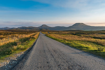 A straight, narrow and empty tarmac road meets at the horizon with the mountains at the isle of sky